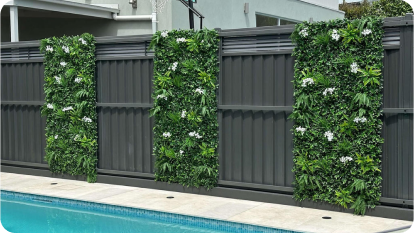 Swimming pool with vertical garden panels featuring lush green foliage and white flowers on a modern dark fence.