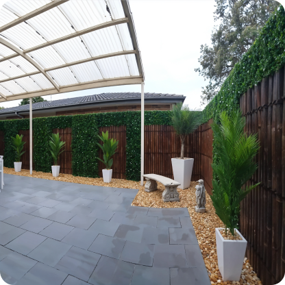 Outdoor patio with dark grey tiled floor, wooden fence covered with greenery, and white planters with tall plants.