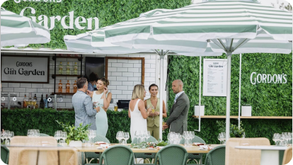 Outdoor garden-themed restaurant with green wall, umbrellas, and socializing patrons.